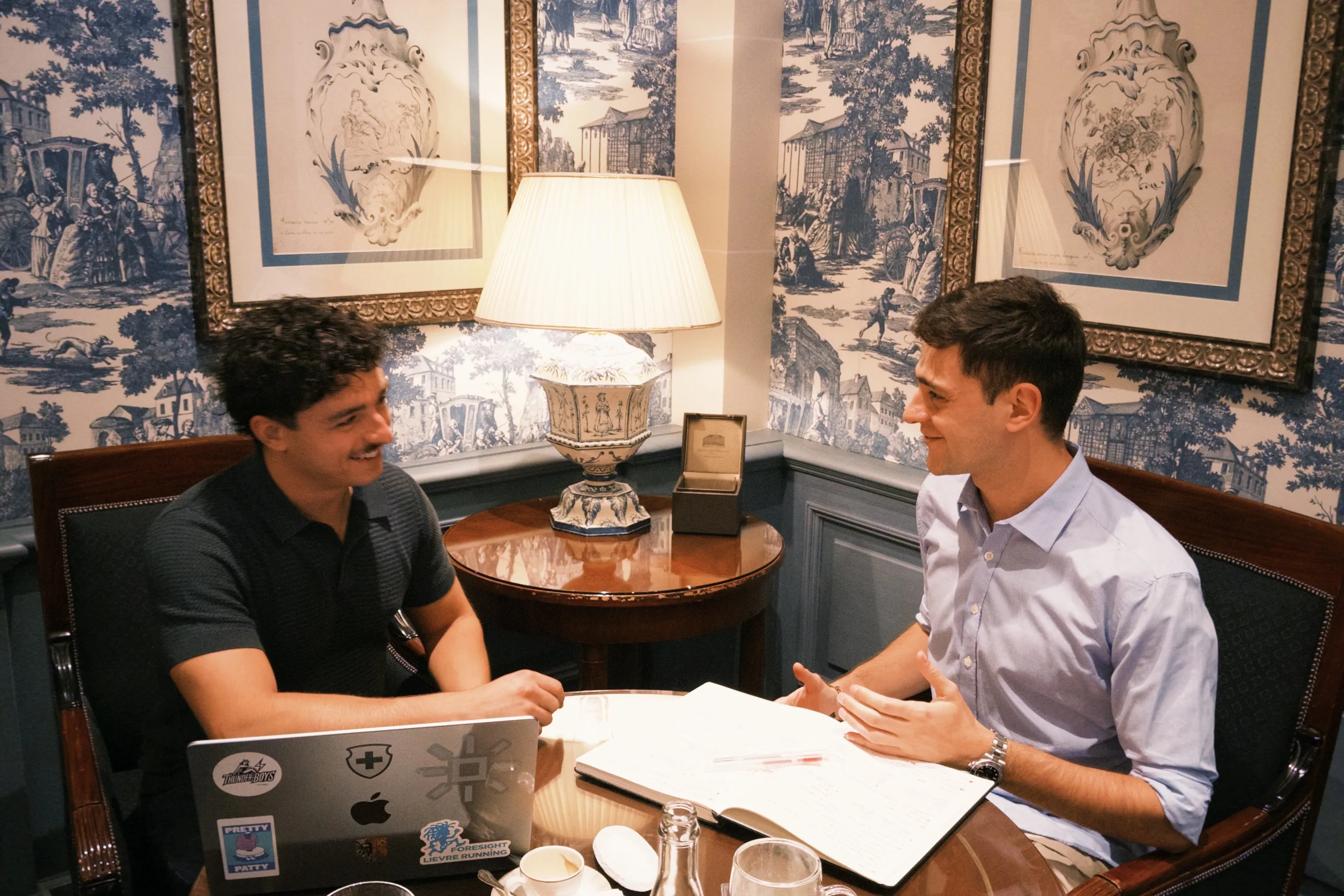Alexandre Pérez et Sullivan Thimotée attablés dans un salon, carnet et ordinateur ouverts.